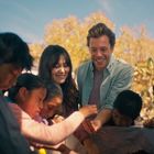 Fröhliche Szene: Ein Mann und eine Frau helfen Kindern, die Erde in einem Garten umgraben; sonniger Tag, Bäume im Hintergrund.