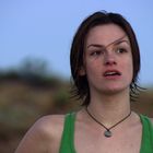 Es gibt keinen Text. Eine Person mit kurzem braunem Haar trägt ein grünes Oberteil und eine Halskette. Hintergrund unscharf.