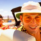 Zwei lachende Personen in einem Cabrio; sonniger Tag, Wüste im Hintergrund. Vordergrund: Mann mit Hut und Sonnenbrille.