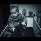 Keine sichtbaren Texte. Eine schwarz-weiß Aufnahme eines schwebenden Babys in einem Kinderbett.