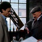 Text: "Made in Germany." Zwei Männer in Mänteln nebeneinander, einer mit Schiebermütze. Verschiedene Flaschen auf dem Tisch.