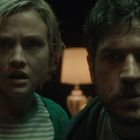 Zwei Personen blicken ernst nach vorn, im Hintergrund eine Tischlampe. Sie wirken konzentriert oder besorgt.