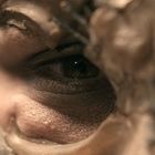 Ein Auge, umgeben von rauer Struktur, teilweise verdeckt, mit unklarer Umgebung.