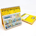 "PEANUTS" von Schulz auf gelbem Tischkalender, Ringbindung, Cartoon mit Iglo und Sprechblasen, daneben Buch auf Gelb.