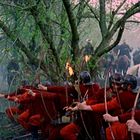 Illustration von Bogenschützen in roten Wappenröcken im Wald, bereit zu schießen. Pferde und Reiter im Hintergrund.