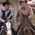 Im Hintergrund steht "House". Zwei Männer in Westernkleidung auf Pferden, lächeln, tragen Cowboyhüte.
