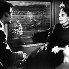 Es ist eine Schwarz-Weiß-Szene in einem Zugabteil: Ein Mann und eine Frau sitzen einander gegenüber. Die Frau hält eine Zigarette.