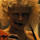 Keine Texte vorhanden. Person mit blondem lockigem Haar, dunklem Lippenstift und schwarzer Farbe im Gesicht.