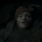 Kein Text. Blasses Gesicht einer verwitterten Puppe mit einem geschlossenen und einem geöffneten Auge, umgeben von dunklem Stoff.