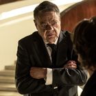 Keine Texte vorhanden. Ein älterer Mann in Anzug steht mit verschränkten Armen und ernstem Gesichtsausdruck vor jemandem.