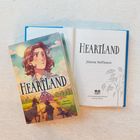 Titel: "Heartland", Autor: Jilanne Hoffmann. Ein Cover zeigt eine Figur auf einer Farm mit Tieren im Hintergrund.