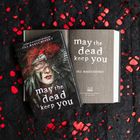 Eine geöffnetes Buch mit der Aufschrift "may the dead keep you" von Jill Baguchinsky. Daneben das Buchcover mit einem geflügelten Gesicht.
