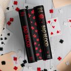 Zwei schwarze Bücher, beschriftet mit "BAD BLOOD" von Jennifer Lynn Barnes, umgeben von Spielkarten und Puzzleteilen.