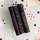 Bücher mit dem Titel "Killer Instinct" von Jennifer Lynn Barnes, umgeben von Spielkarten mit Herzen und Kreuz-Symbolen.