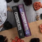 Zwei Bücher mit "CURSEBREAKER" auf dem Buchrücken. Umgeben von dekorativen Rosen und einem Stoff.