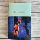 „The Nutcracker, Alexandre Dumas“ in goldener Schrift. Illustration eines Kindes mit einem Nussknacker im Kerzenlicht.
