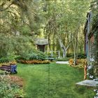 „From virtually any approach“ – ein grüner Garten mit Bäumen, einer Hütte, einem Weg und einem blauen Schubkarren.