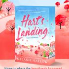 Text: "Hart's Landing", "Trouble's coming back home...", "Home is where the heartbreak happened... and where she might finally heal." Darstellung: Buntes Cover mit Bäumen und Häusern.