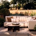 „Styling with Intention“: Außenmöbel, helle Couch, Holztisch, Topfpflanze, Hintergrund mit Bäumen und Wiese.