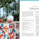 Links ein Tisch mit einer Tischdecke mit roten und blauen Motiven, Tomaten und eine blaue Kanne. Rechts steht: "Tablecloth".