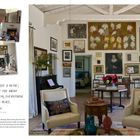 "Art doesn’t decorate a home; it defines it." Wohnzimmer mit Gemälden, Fotos, einem Kamin, Sesseln und einem Tisch mit Blumen.