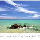 "Küstenimpression" steht über einer Szene mit klarem Wasser, Felsen im Vordergrund und blauem Himmel mit langen Wolken.
