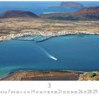 La Graciosa. Eine Küstenlandschaft mit Hafen, in der Ferne Berge und ein blaues Meer. Kalender mit März-Datum.