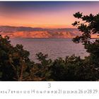 Abendstimmung. Kalender zeigt März. Sonnenuntergang über einem See mit Bäumen im Vordergrund und Bergen im Hintergrund.