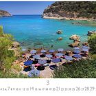 "Anthony Quinn Beach". Ein Strand mit türkisem Wasser, Menschen schwimmen, Felsen und Bäume, gestreifte Sonnenschirme.