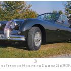 Jaguar XK40. Kalendarium mit den Zahlen 1 bis 31, der März ist markiert. Ein klassisches Auto steht auf einer Wiese.