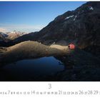 "Panorama im Licht." Berglandschaft mit einem roten Haus, klarer Himmel, Felsen und ein kleiner See.