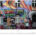 Graffiti-Wand mit bunten Figuren und knalliger Schrift. Kalender unten zeigt September mit hervorgehobener Sieben.