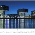Kranhäuser, Kalender zeigt März, zeigt moderne Architektur am Fluss bei Nacht, beleuchtet, mit spiegelndem Wasser.