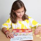 Zahlen von 1 bis 9 in einem Spielset. Ein Mädchen spielt damit am Tisch, trägt eine gelb-weiß gemusterte Bluse.