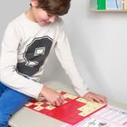 Ein Kind ordnet Zahlenkarten mit einer Multiplikationstabelle. Es trägt einen Pullover mit einer großen "9".