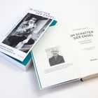 Zwei Bücher mit dem Titel "Im Schatten der Engel: Leonard Cohen – eine Biografie". Cover zeigt Mann im Trenchcoat.