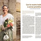 Con le nostre indiane e senza grembiule. Frau in historischem Kostüm aus Brokat, mit Blumenstrauß, steht vor einer Steinmauer.