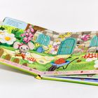 Text oben: "Dort drüben auf der Wiese... schlaue Maus!"  
Text unten: "Milly Maus hat heute viel zu tun..."  
Illustration: Maus in buntem Garten mit Blumen und Türen.