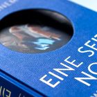 Der Text „EINE SEITE NOCH“ steht auf einem blauen, strukturierten Buchdeckel mit kreisförmigem Ausschnitt.