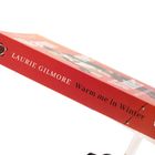 "Buchrücken mit Text: 'LAURIE GILMORE Warm me in Winter' auf rotem Hintergrund, im Vordergrund ein aufgeschlagenes Buch."