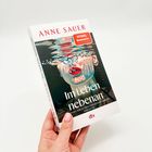 Text: „ANNE SAUER“, „Im Leben nebenan“, „ROMAN“, „dtv“. Illustration: Gesicht unter Wasser mit Luftblasen. Buch in Hand gehalten.
