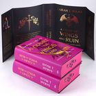 Zwei pinke Bücher mit dem Titel "A Court of Wings and Ruin" von Sarah J. Maas. Ein offener schwarzer Umschlag zeigt ein Schwert und Flügel.