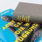 Text: "Kathrin Fischer ACHTSAM GEHT DIE WELT ZUGRUNDE". Ein graues Buch liegt auf einem blauen Buchcover mit Buddha-Bild.