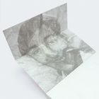 Ein grau-schwarzer Porträtabdruck auf gefaltetem Papier. Ein Gesicht mit sanften Konturen und Details.