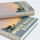 „NACH HAUSE KOMMEN“ auf einem Buchcover mit einem Lastwagen in einer Landschaft bei Sonnenuntergang.