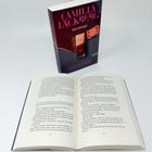 Ein Buchcover mit "CAMILLA LÄCKBERG REVENGE". Offenes Buch zeigt Text auf den Seiten 152 und 153.