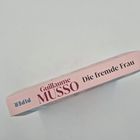 "Guillaume MUSSO Die fremde Frau" auf einem Buchrücken, rosa Hintergrund, "PIPER" seitlich angezeigt.
