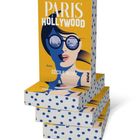„PARIS HOLLYWOOD“ von Cécile Mury. Illustration einer Frau mit Sonnenbrille, stapelweise Bücher, gelber Hintergrund.