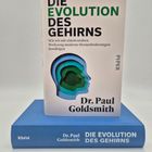 Buchtitel: "Die Evolution des Gehirns" von Dr. Paul Goldsmith. Cover mit farbiger Gehirn-Silhouette. Buch liegt auf blauem Band.