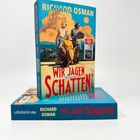 „Richard Osman: Wir jagen Schatten. Kriminalroman“. Ein Buch mit einer Illustrationsfigur auf einem Stuhl vor einem Landschaftshintergrund.